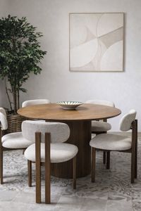 Round wooden dining table with upholstered chairs in Mallorca showroom with soft neutral tones and natural materials Round wooden dining table with upholstered chairs in Mallorca showroom with soft neutral tones and natural materials