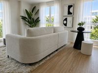 Sala de estar contemporánea en Es Molinar con sofá curvo claro, detalles en blanco y negro, luz natural y ambiente mediterráneo