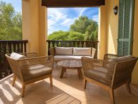 Covered Mediterranean terrace in Bendinat Golf with woven outdoor lounge furniture, natural wood coffee table and relaxed holiday atmosphere surrounded by pine trees on Mallorca.