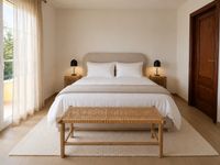 Minimal Mediterranean bedroom in Bendinat Golf with upholstered bed, white cotton bedding, natural linen plaid, woven bench and soft neutral styling on Mallorca.