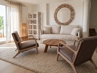 Relaxed family living room in Bendinat Golf with natural linen sofa, wooden lounge chairs, soft wool rug and calm Mediterranean Relaxed family living room in Bendinat Golf with natural linen sofa, wooden lounge chairs, soft wool rug and calm Mediterranean
